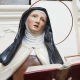 Riconosciamo, incastrata tra banchi rovesciati, la statua lignea di Teresa D�Avila, vestita in abiti monacali, con lo sguardo in contemplazione e un testo sacro aperto nella mano sinistra 